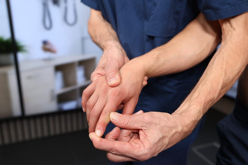 The examiner passively flexes the index finger's distal joint while supporting the finger.